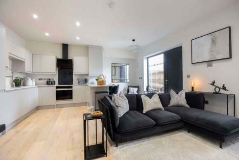 Spacious living room with black sofa, modern decor, and open kitchen area.