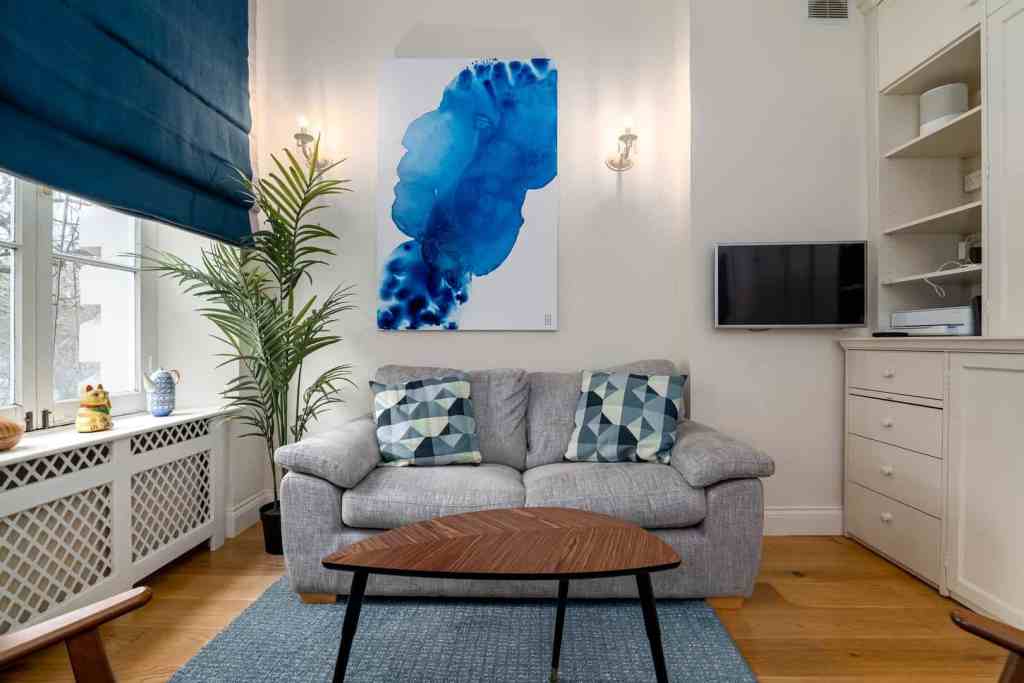 Cozy living room with gray sofa, abstract blue art, and natural light.