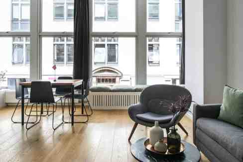 Bright living room with large windows, sofa, and dining area in a serviced apartment.