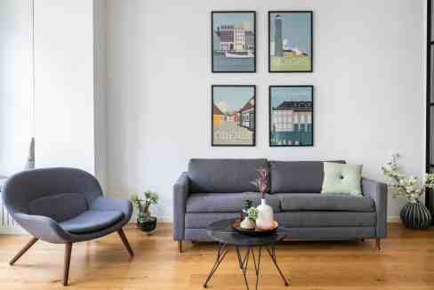Modern living room with gray sofa, armchair, and artwork on white wall.