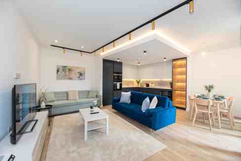 Modern open-plan living room with sofa, dining area, and kitchen in a serviced apartment.