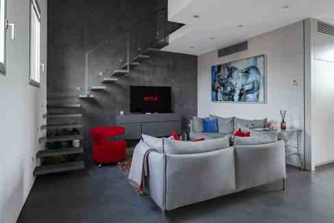 Modern living room with gray sofas, red armchair, and staircase in Florence apartment.