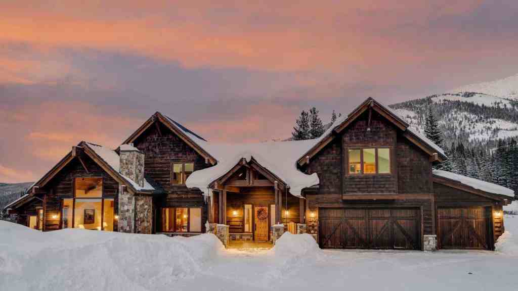 Elegant mountain villa with snow-covered landscape and warm lighting at sunset.