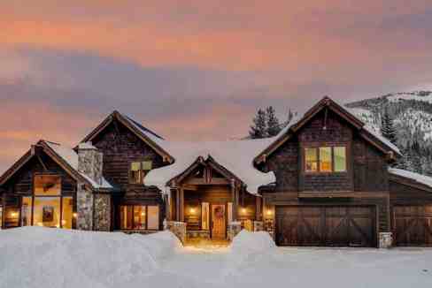 Elegant mountain villa with snow-covered landscape and warm lighting at sunset.