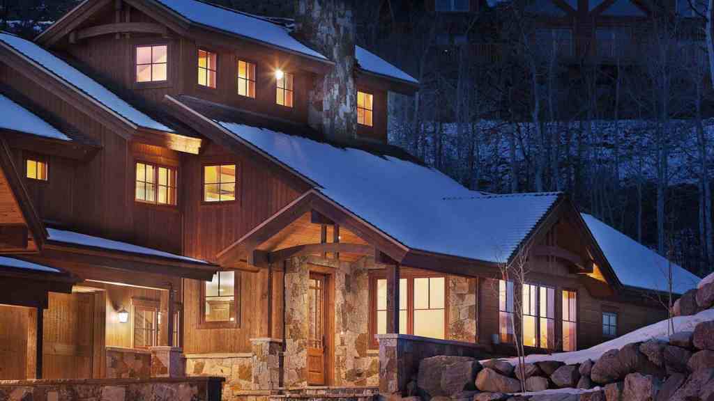 Cozy mountain cabin with warm lights and snow-covered roof at night.