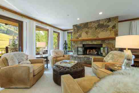 Cozy living room with large windows, stone fireplace, and plush seating.