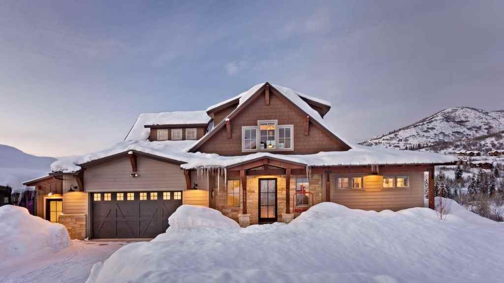 Snow-covered mountain cabin with warm interior lights at dusk.
