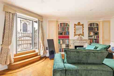 Luxurious living room with large window, green velvet sofa, and ornate mirror.