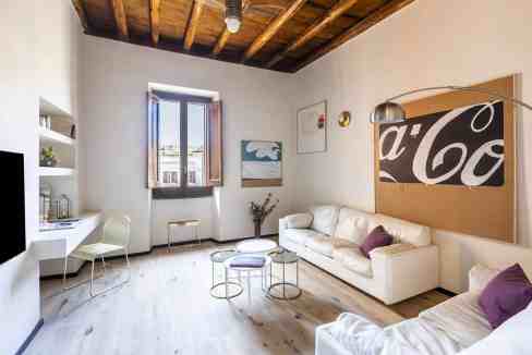 Modern living room with white sofas, wooden ceiling, and large window.
