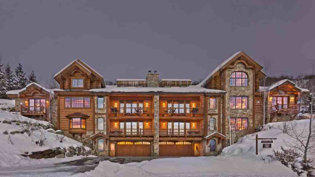 Elegant mountain lodge with snow-covered surroundings and warm interior lights.