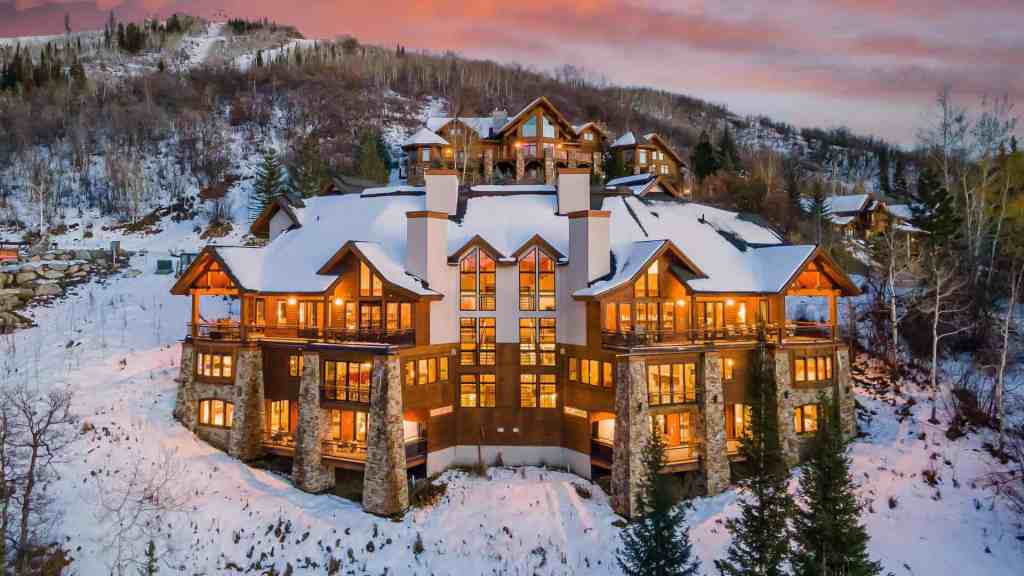 Elegant mountain lodge with snow-covered roof and warm lighting at sunset.