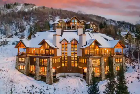 Elegant mountain lodge with snow-covered roof and warm lighting at sunset.