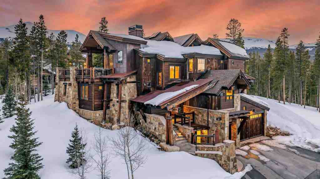 Luxury mountain lodge with rustic wood and stone design in a snowy landscape.
