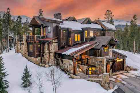 Luxury mountain lodge with rustic wood and stone design in a snowy landscape.