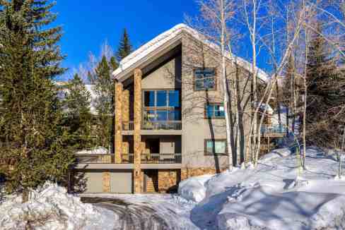 Contemporary mountain cabin in snowy landscape with trees and blue sky.
