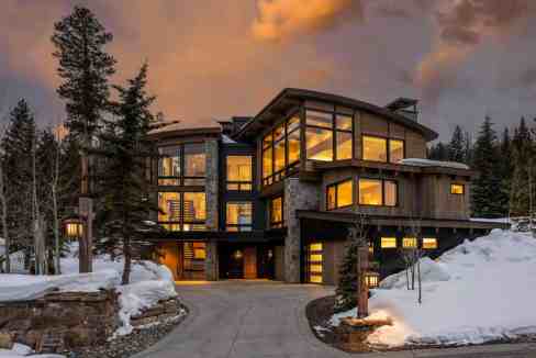 Contemporary mountain house with large glass windows and snow-covered landscape.