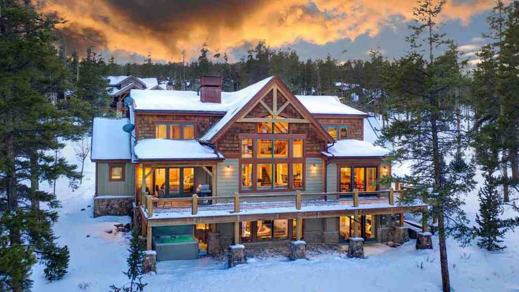 Elegant mountain chalet with snow-covered roof and large windows at sunset.