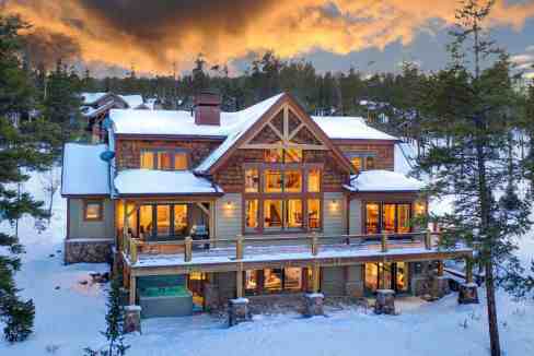Elegant mountain chalet with snow-covered roof and large windows at sunset.
