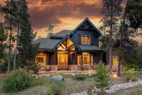 Elegant mountain cabin with warm lighting and surrounding trees at sunset.