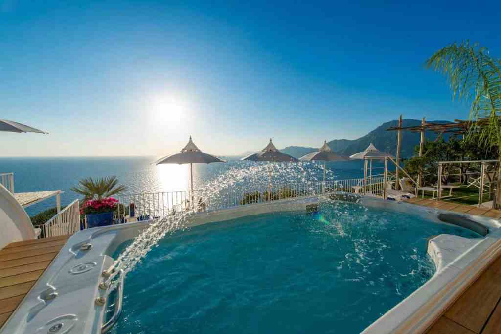 Luxury hot tub overlooking Amalfi Coast with ocean view and umbrellas.