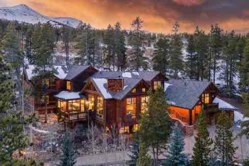 Luxury lodge in snowy forest with mountain backdrop at sunset.