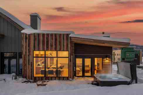 Modern alpine villa with large windows and hot tub in snowy landscape.