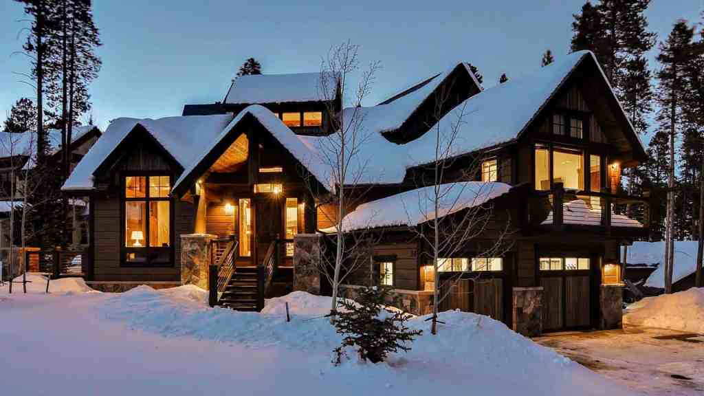 Luxury chalet with snow-covered roof and warm interior lights at dusk.