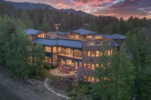Elegant mountain lodge with large windows and outdoor patio at sunset.
