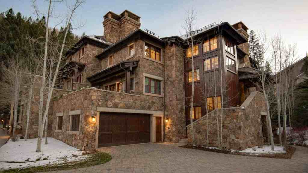 Elegant mountain villa with stone facade and large windows in winter setting.