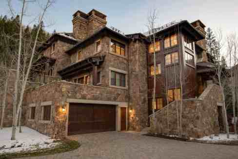 Elegant mountain villa with stone facade and large windows in winter setting.