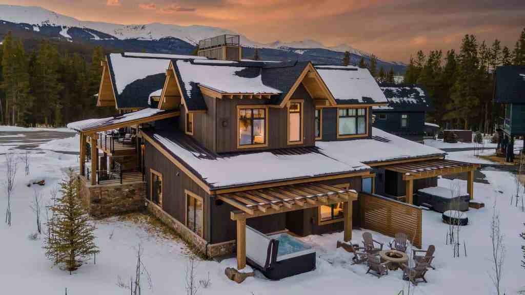 Elegant mountain cabin with snow-covered roof and outdoor seating area at sunset.