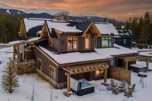 Elegant mountain cabin with snow-covered roof and outdoor seating area at sunset.