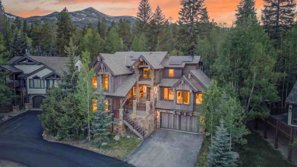 Elegant mountain house surrounded by trees at sunset with mountain views.