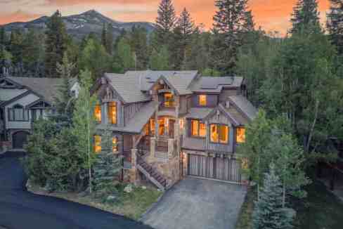 Elegant mountain house surrounded by trees at sunset with mountain views.