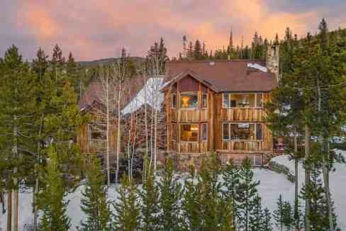 Cozy mountain lodge surrounded by snow and pine trees at sunset.