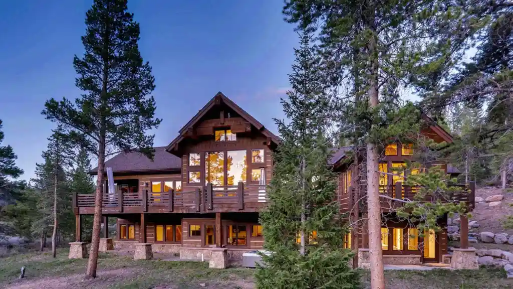 Luxury mountain cabin with large windows in a forest setting.