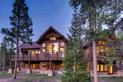 Luxury mountain cabin with large windows in a forest setting.