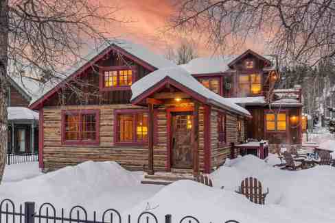 Cozy mountain cabin with snow-covered yard and warm interior lights.