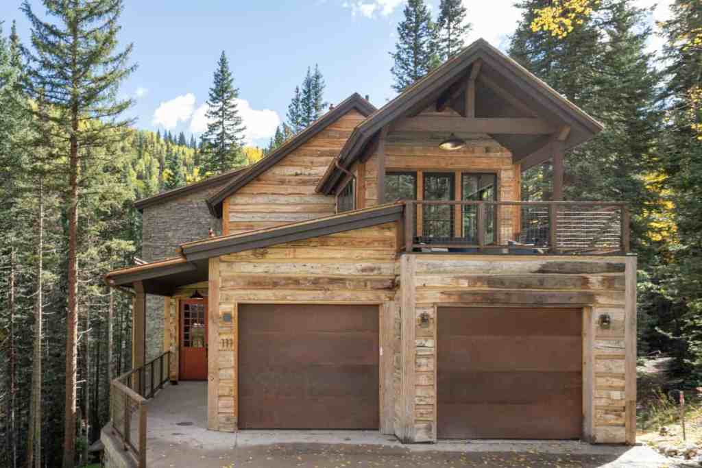Rustic mountain chalet with wooden accents and garage in forest setting.