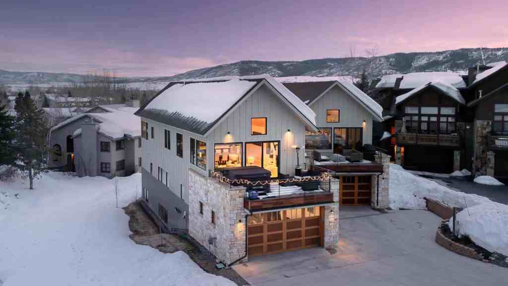Snow-covered chalet with warm interior lights in a mountain setting.