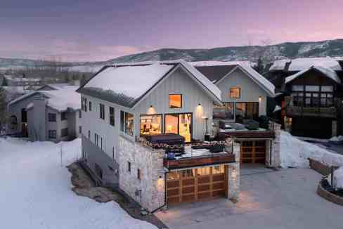 Snow-covered chalet with warm interior lights in a mountain setting.