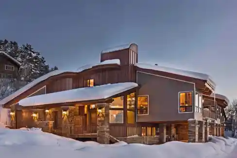 Elegant mountain cabin with snow-covered roof and warm interior lights.