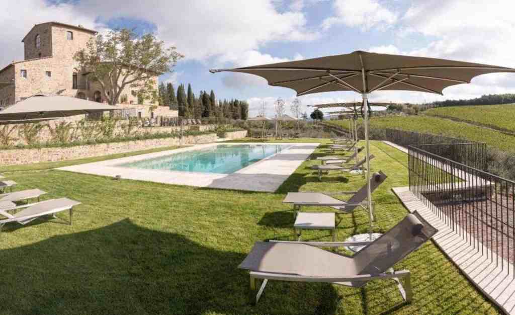Scenic view of a swimming pool with sun loungers and umbrellas in Chianti countryside.