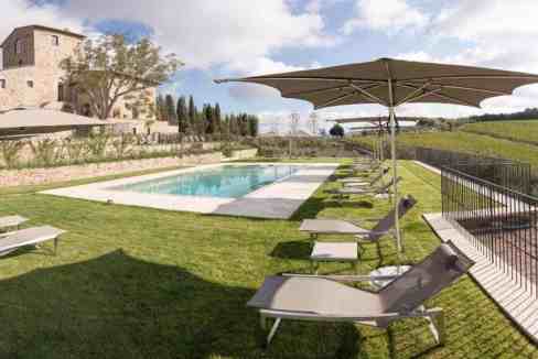 Scenic view of a swimming pool with sun loungers and umbrellas in Chianti countryside.