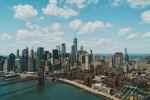 New York City skyline with skyscrapers and Brooklyn Bridge under blue sky.