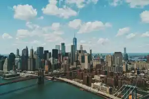 New York City skyline with skyscrapers and Brooklyn Bridge under blue sky.