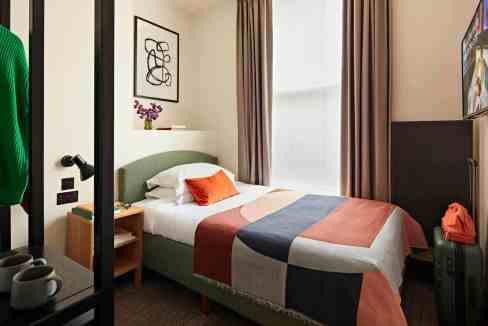 Modern hotel room with bed, artwork, and window in Fitzrovia Studio Collection.