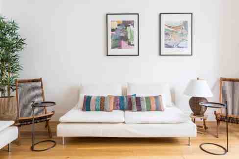 Contemporary living room with white sofa, wooden chairs, and abstract art.