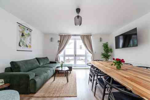 Modern living room with green sofa, wooden dining table, and balcony view.