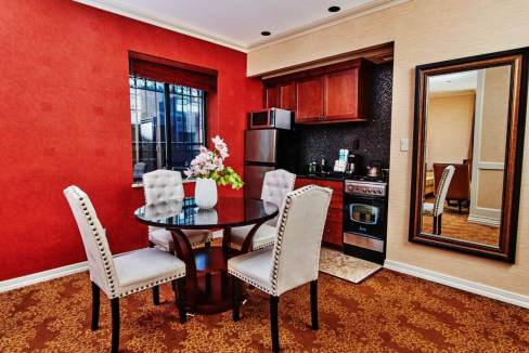 Modern serviced apartment dining area with red accent wall and four upholstered chairs.